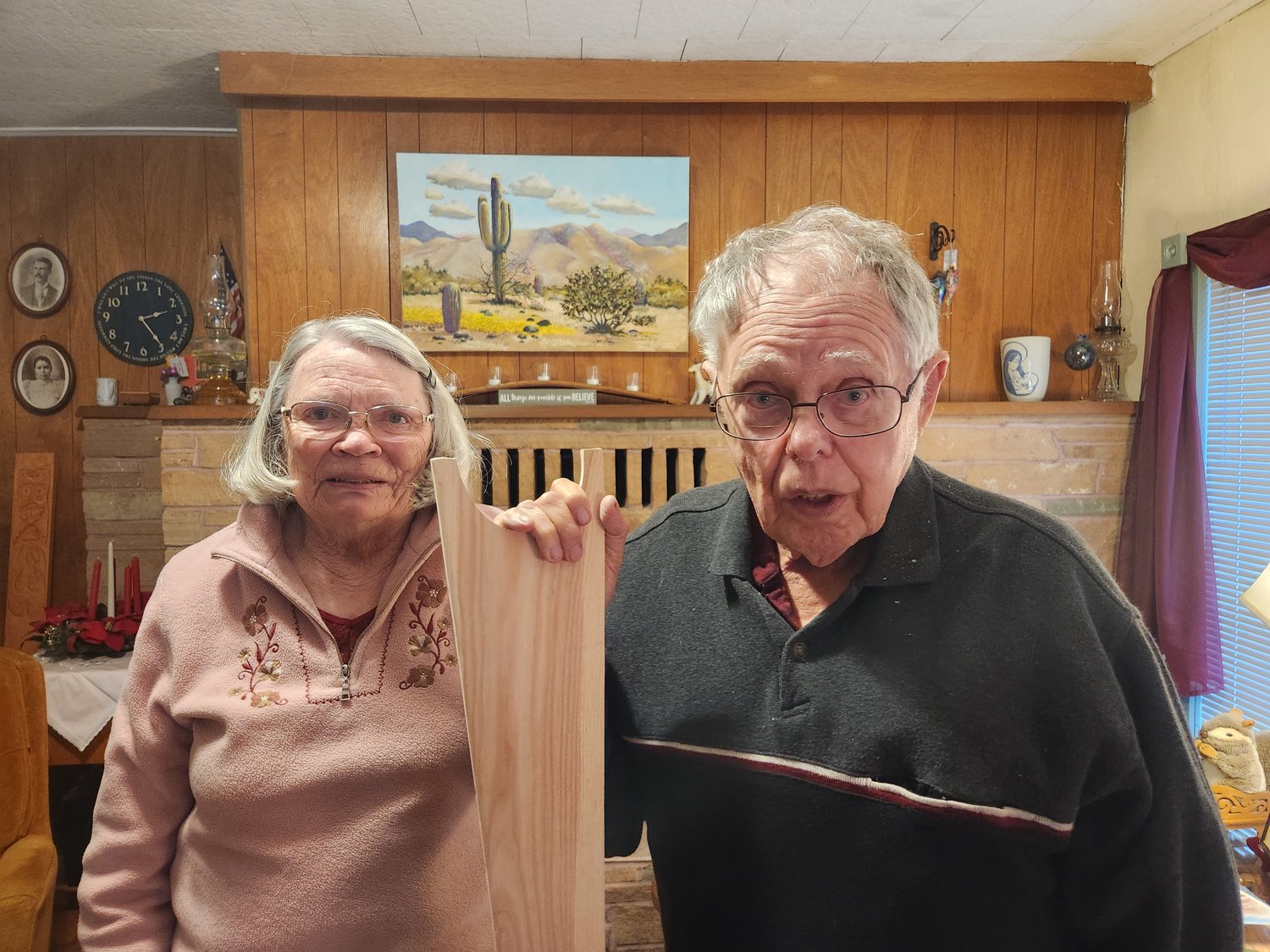 20221212-151959-0 Mary and Charlie Funk holding the Chinook paddle with a painting by Charlie on the wall behind them